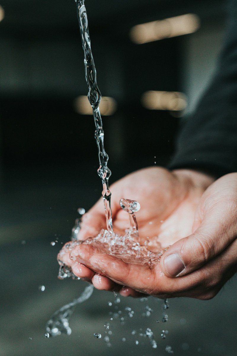 Mains en coupe sous un filet d'eau sur un fond sombre