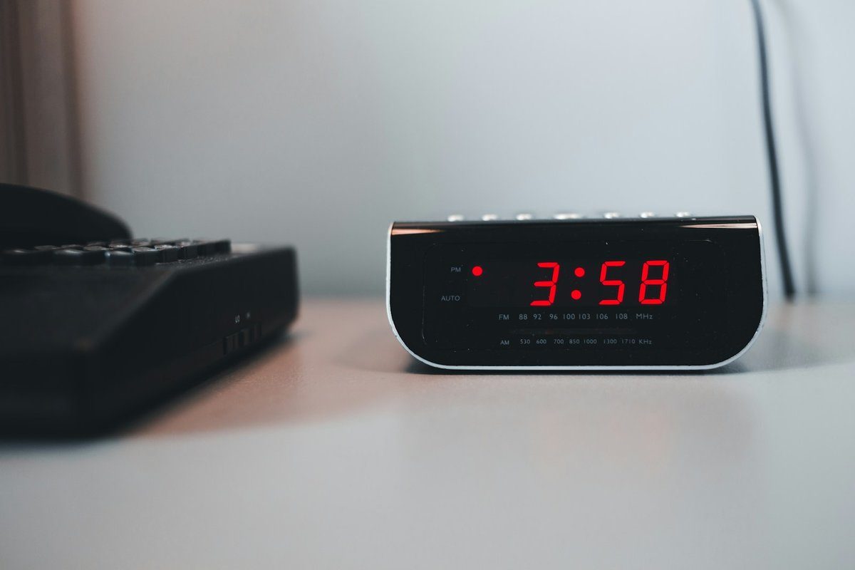Radio-réveil affichant 3:58 en chiffres rouges sur une table de chevet