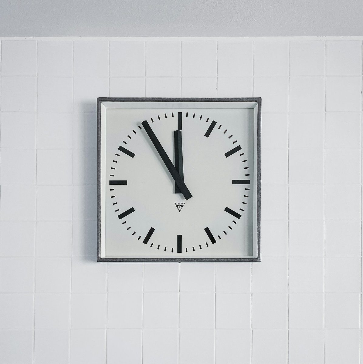 Horloge murale carrée accrochée sur un carrelage blanc