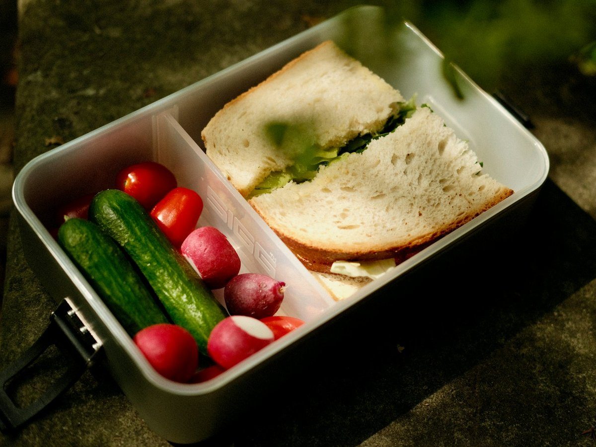 Boîte à repas métallique ouverte avec un sandwich et des crudités