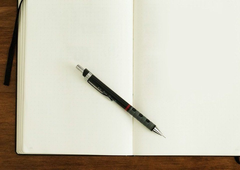 Carnet ouvert aux pages vierges avec un critérium posé dessus, sur une table en bois