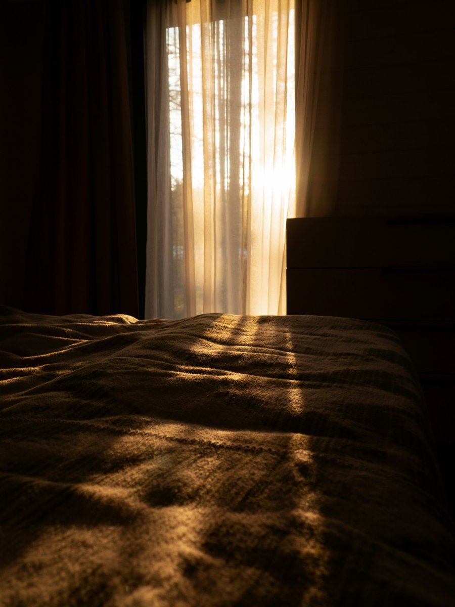 Soleil du matin filtrant à travers des voilages sur un lit dans la pénombre